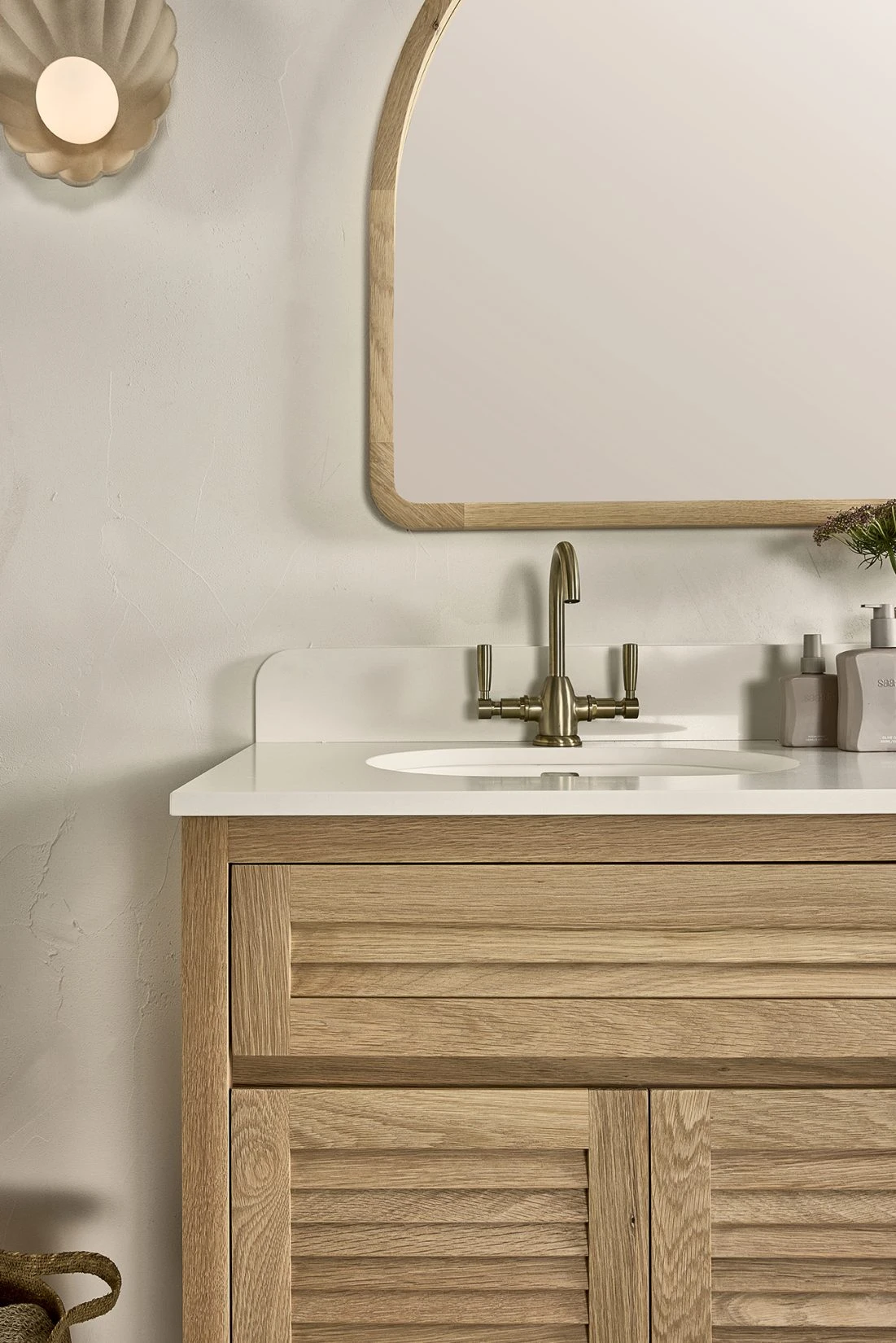 A bathroom vanity with a splashback underneath a curved timber frame mirror.